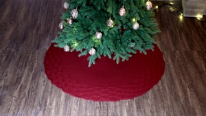 Macro detail of deep red cable-knit Christmas tree skirt on a dark wood floor