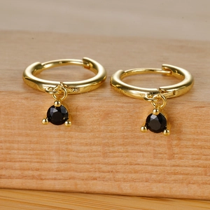 Detail of gold huggie earrings with round black zircon pendants and three-prong setting