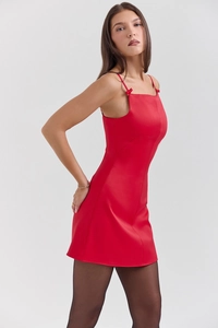 Détail d'une robe courte rouge à bretelles ajustée sur un fond gris minimaliste