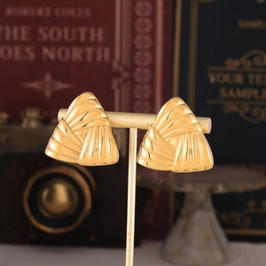 Modern geometric triangle earrings in gold-plated steel featuring ribbed texture on a stand