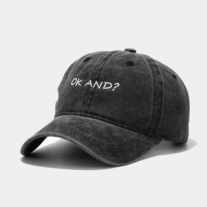 Detail of white OK AND? embroidery on washed charcoal cotton baseball cap surface