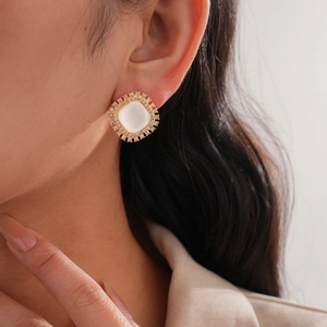 Close-up of golden square stud earring with white resin stone and rhinestone accents