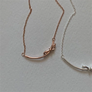 Detailed view of silver and rose gold bow necklaces on a light grey textured background
