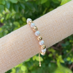 Detail of 18K gold-plated beads and faux pearls bracelet on a soft fabric display