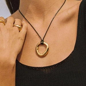 Close-up of a vintage golden irregular ring pendant on a black cord necklace and rings