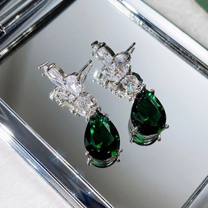 Macro shot of teardrop emerald earrings with sparkling AAA zircon inlay on silver base