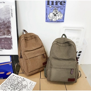 Brown and army green canvas backpacks with front zip pockets in a lifestyle setting