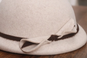 Detail of wool texture and decorative knot on beige beret hat over wood background