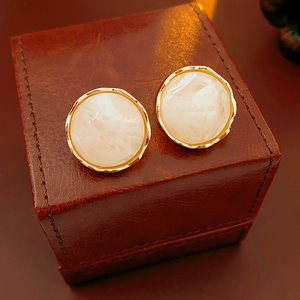 Detailed close-up of vintage gold round earrings with white marble texture on leather