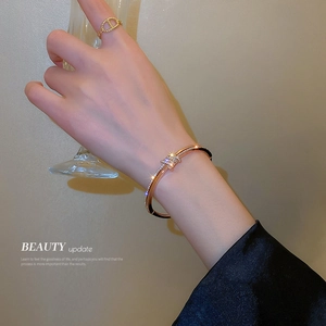Elegant rose gold knot bracelet with diamonds and matching ring on a hand holding a glass