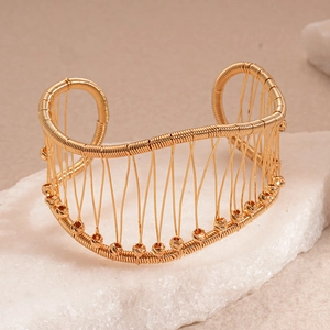 Détail d'un bracelet manchette doré tressé avec perles métalliques sur une pierre blanche