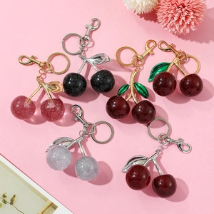 Flat lay macro of cherry-shaped resin keychains with glitter and gold metal leaf details