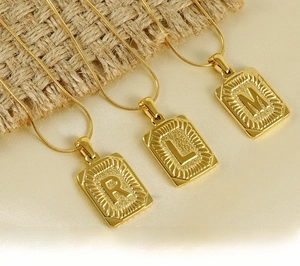 Détail macro de pendentifs carrés en acier inoxydable plaqué or 18K avec lettres