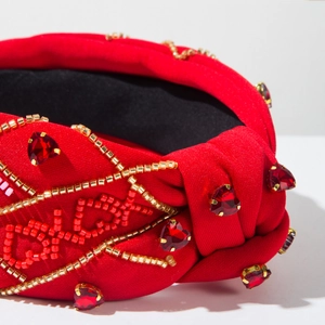Dettaglio macro della fascia rossa con nodo, perline LOVE e strass a forma di cuore