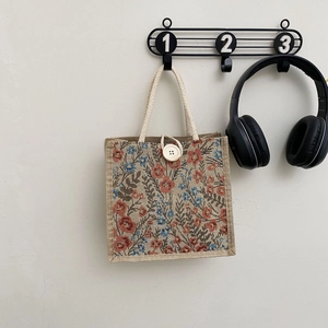 Close-up of linen floral handbag with woven handles and white button closure detail