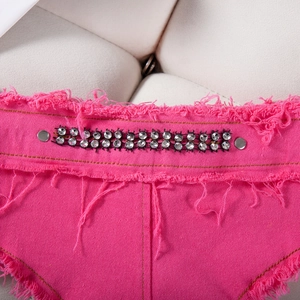 Dettaglio di pantaloncini in denim rosso rosa con strass e bordi sfilacciati