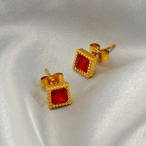 Square red zircon stud earrings with golden beaded edges on soft satin fabric background