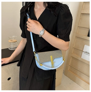 Detail of light blue crossbody bag with woven straw flap and gold metal twist lock
