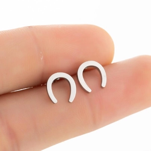 Close-up of silver U-shaped horseshoe earrings held by hand showing small size scale