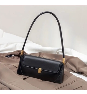 Close-up of black baguette underarm bag with gold buckle on brown suit and white fabric