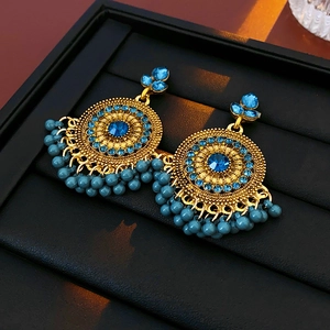 Dettaglio di orecchini vintage dorati con pietre blu e nappine di perline etniche