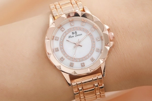 Close-up of women's rose gold watch with rhinestone markers and mother of pearl dial