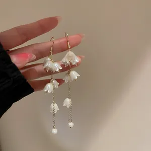 Détail de boucles d'oreilles muguet en acrylique avec longues franges dorées et perles