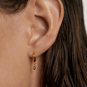Close-up of golden teardrop pendant earring worn by a model in a minimalist style