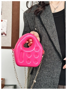 Detail of pink jelly mini bag with gold chain strap held by a model in a grey blazer