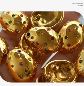 Macro detail of gold oval earrings with colorful rhinestones held in a hand