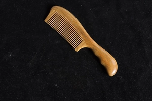 Close-up of natural sandalwood comb with fine teeth and smooth handle on black velvet