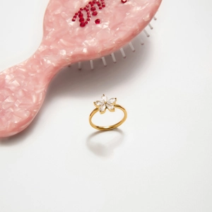 Elegante anello a fiore dorato con cinque zirconi bianchi su marmo rosa raffinato