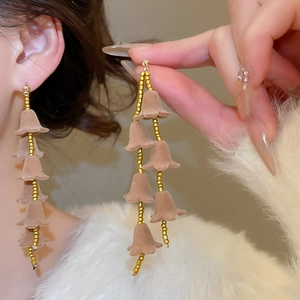 Gros plan de boucles d'oreilles fleurs floquées avec pompons de perles dorées sur mannequin