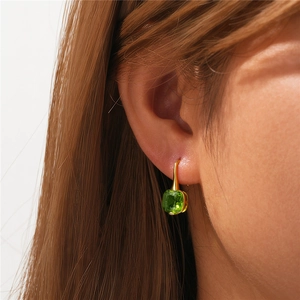 Close-up of elegant gold hook earring with a square-cut green gemstone on model