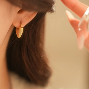 Macro shot of minimalist brushed gold heart hoop earrings worn for a sleek style