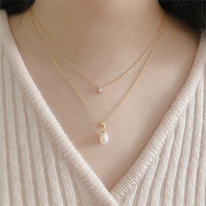 Detail of layered gold necklace with round zircon and teardrop pearl on model