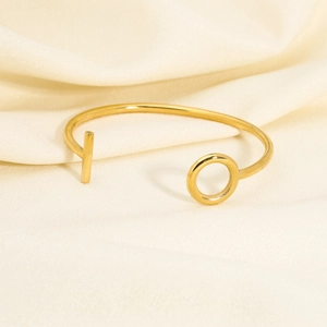 Detail of a minimalist gold open bangle with geometric ends on a soft textured fabric