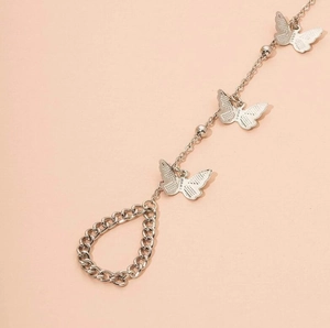 Détail de la chaîne de main papillon argentée avec perles sur fond rose pastel