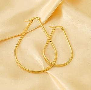 Close-up of polished gold-tone teardrop hoop earrings on a silk satin fabric background