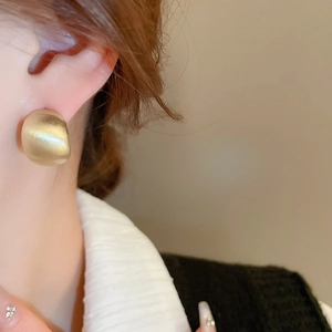 Detail of matte gold chunky C-shaped earrings worn by a model for a stylish metal look