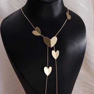Detail of long gold necklace featuring layered textured heart pendants on black display