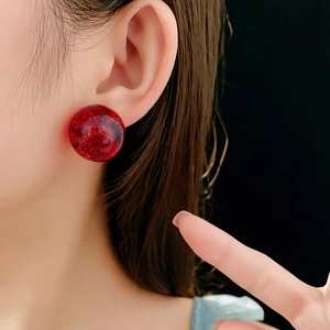 Close-up of a woman wearing red resin ball stud earrings with gold foil texture
