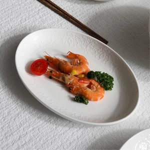 Oval white embossed ceramic serving plate with cooked shrimp on a textured tablecloth
