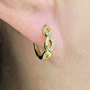 Detailed close-up of golden infinity pavé huggie hoop earrings worn on a model's ear