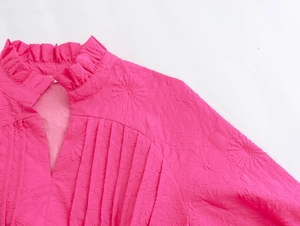 Detail of hot pink mini dress featuring textured floral fabric and ruffle stand collar
