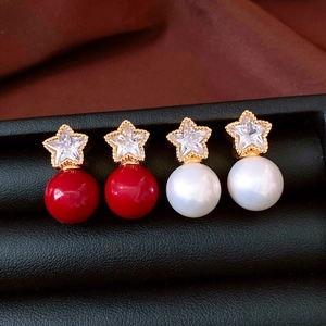 Detailed macro view of 18K gold plated star earrings with red and pearl beads on black leather