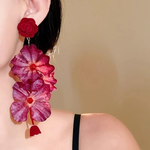 Primo piano di orecchini a rosa in tessuto rosso con lunghe nappe su una modella