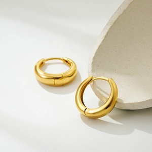 Close-up of polished 18K gold hoop earrings on natural stone aesthetic background