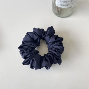 Close-up of navy blue satin scrunchie with elegant pleated fabric on a clean background