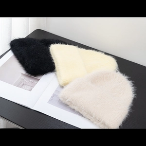 Three fluffy knit beanies in black, yellow, and beige on a stylish wood surface